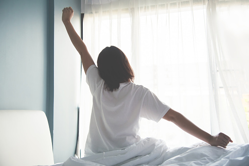 Person stretching sitting on the side of their bed after waking up