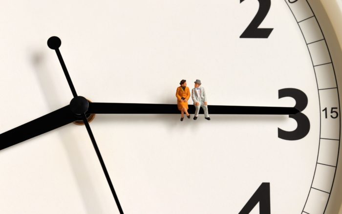 Miniature woman and man sitting on the small hand of a clock pointing