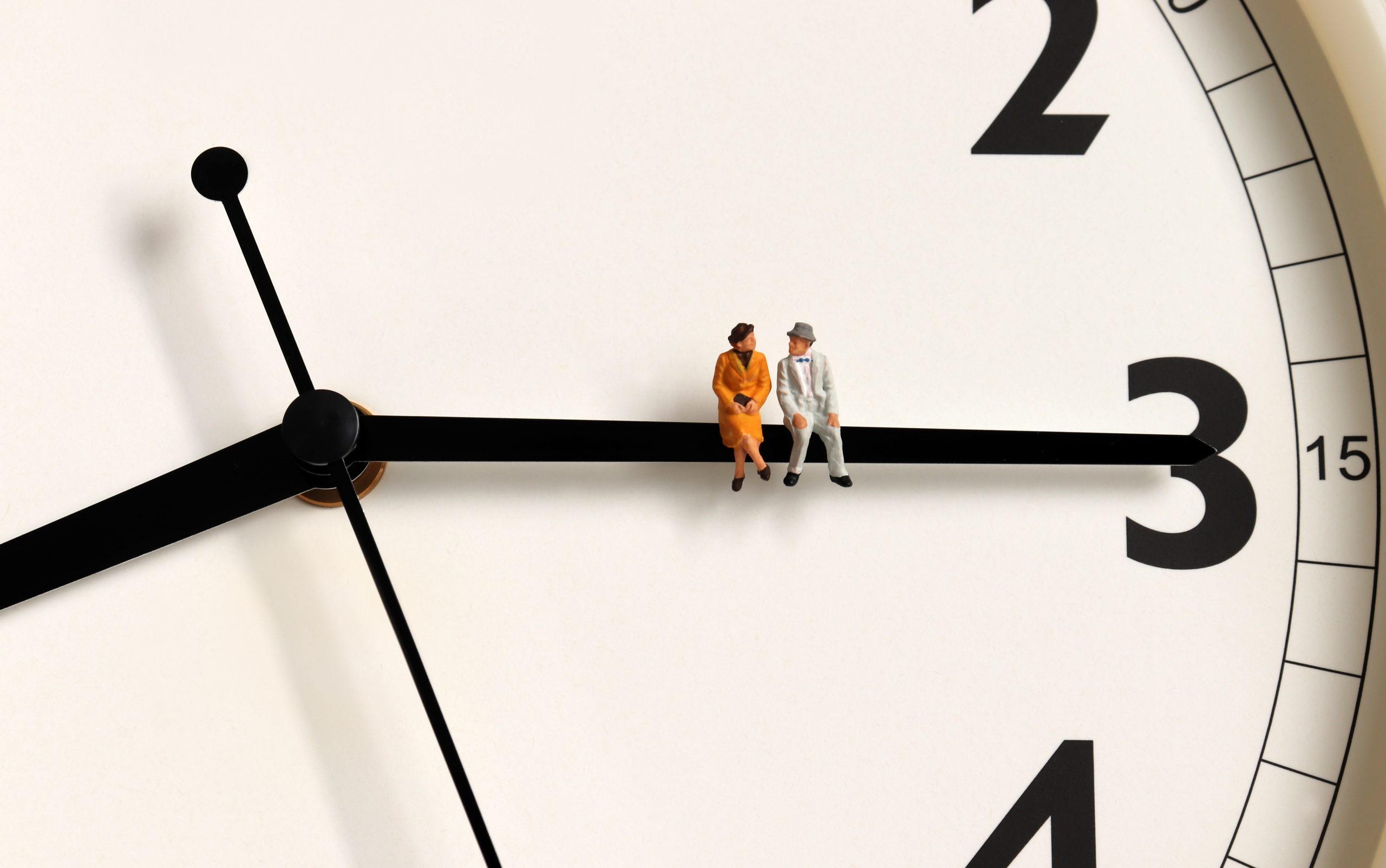 Miniature woman and man sitting on the small hand of a clock pointing
